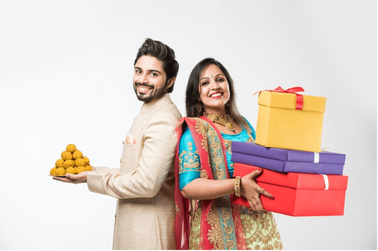 2 models dressing in indian diwali festival having gifts and foods in thier hands